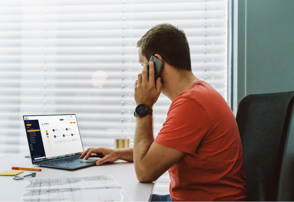 Installer sitting at a desk using his laptop to log into Set Pro by Somfy software while he is on the phone.